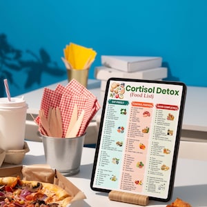 May include: A tablet displays a "Cortisol Detox (Food List)" with food categories. A pizza in a box, a slice of pizza, and a drink with a straw are on a white table. Napkins and utensils are in a metal bucket. A blue background completes the scene.