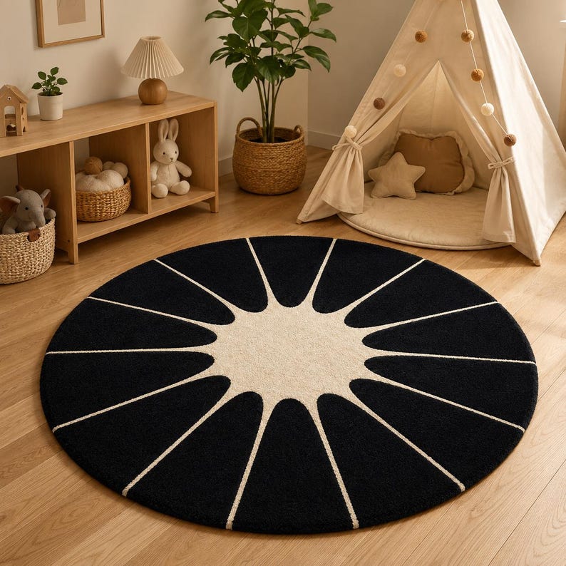 May include: A circular area rug featuring a black background with a large, central cream-colored sunburst pattern. The design consists of a solid cream circle in the middle with radiating, petal-like cream lines extending toward the edge.