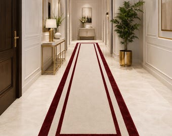 May include: A long rectangular runner rug featuring a solid cream-colored center panel framed by two distinct, bold dark red borders. The rug is positioned centrally along a polished light-colored floor in a bright, symmetrical hallway interior.
