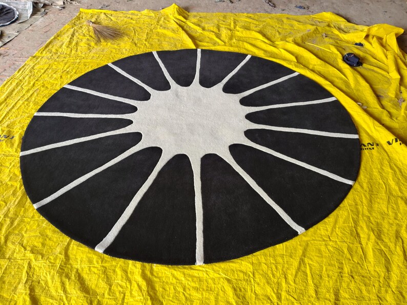 May include: A circular rug featuring a high-contrast design with a solid black background and a central white star-like shape. The white pattern extends from the center toward the outer edge in twelve distinct, elongated, tapered rays.