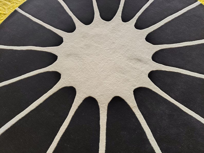 May include: A circular rug featuring a high-contrast design with a central off-white starburst shape that extends outward into long, thin, curved points, set against a solid black background that fills the remaining space of the circle.