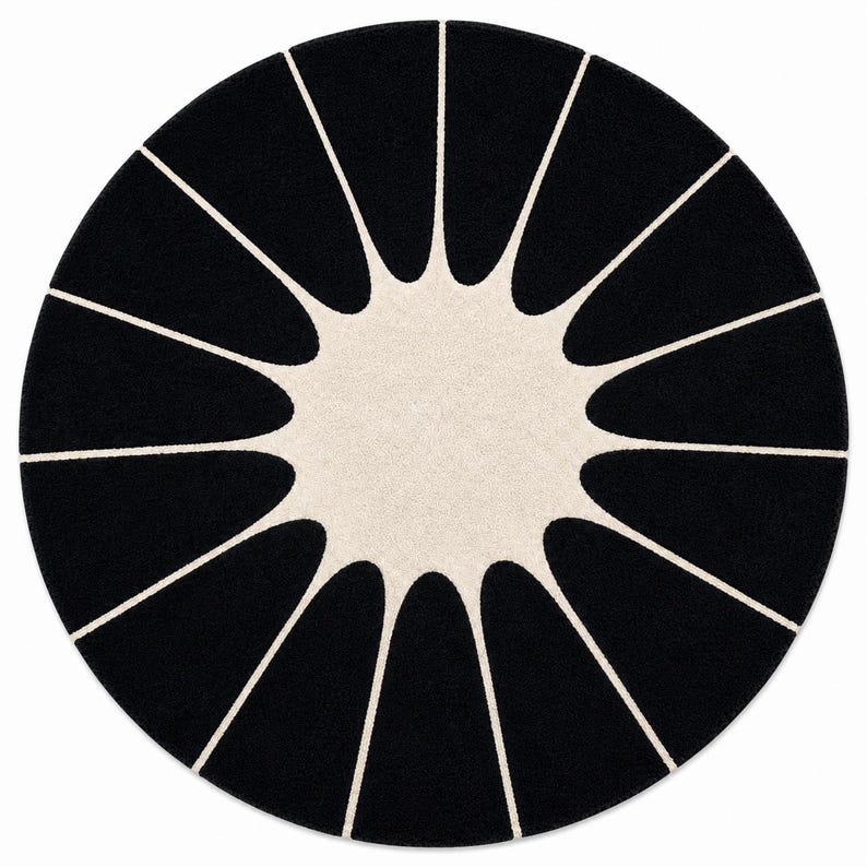 May include: A circular area rug featuring a high-contrast design with a solid black background and a central cream-colored starburst pattern. The cream shape extends outward with twelve pointed rays that reach toward the edge of the rug.