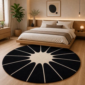 May include: A large circular area rug featuring a bold, high-contrast design with a central cream-colored sunburst pattern radiating outward into long, petal-like shapes against a solid black background, creating a striking geometric focal point.