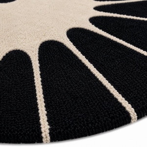 May include: A circular rug featuring a high-contrast design with a central cream-colored circle radiating outward into long, pointed black petals. The surface has a dense, tufted texture with clearly defined cream borders separating the black sections.