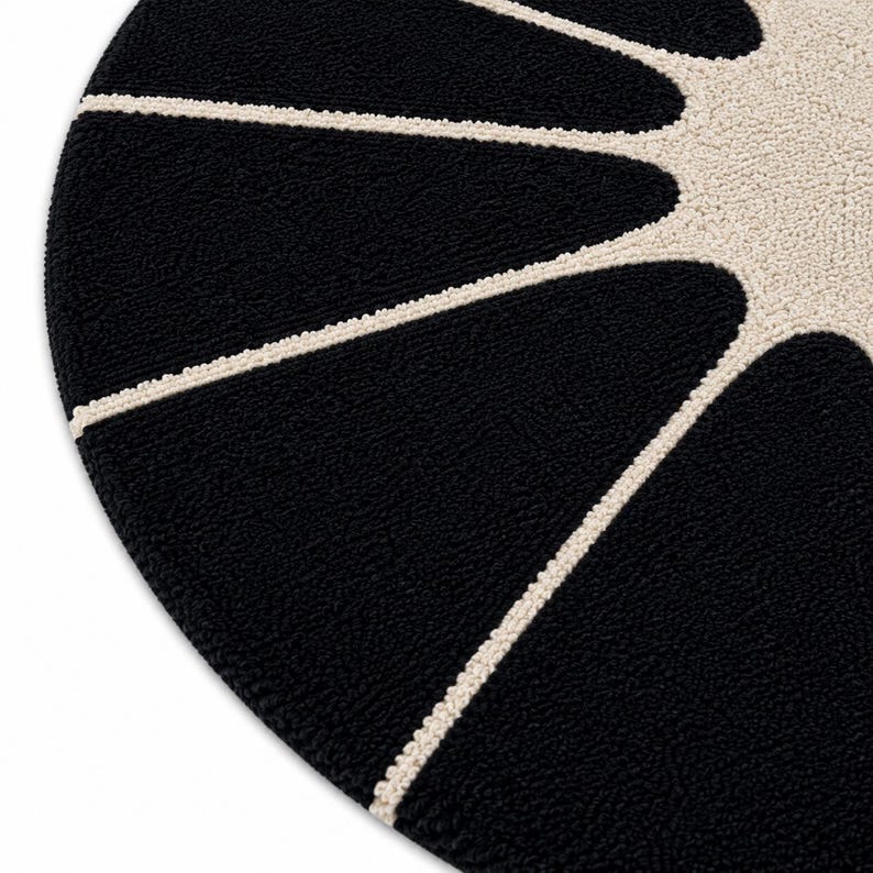 May include: A circular rug featuring a high-pile, tufted texture. The design consists of a solid black background with a cream-colored sunburst pattern radiating from the center, creating distinct, elongated, petal-like shapes.