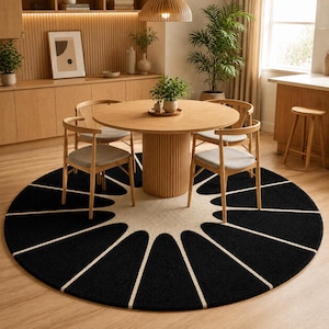 May include: A large circular area rug featuring a bold black and cream sunburst or petal pattern. The rug has a thick, textured pile and is positioned on a light wood floor beneath a round wooden dining table with four matching chairs.