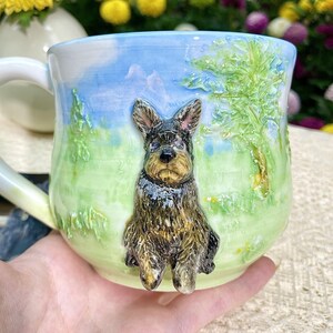 May include: A ceramic mug with a detailed, three-dimensional sculpture of a dog. The mug features a landscape design with a blue sky, green grass, and trees. The dog is black and brown, with a textured coat. The handle is white.