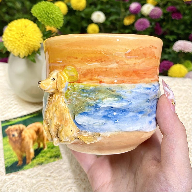 May include: A ceramic mug featuring a golden retriever dog design. The mug has a painted scene of a sunset over the ocean, with the dog sculpted on the side. The color palette includes shades of orange, blue, and tan.