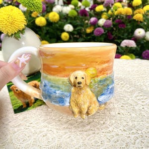 May include: A ceramic mug featuring a golden retriever on a beach scene with a sunset design. The mug has a white handle and a sculpted dog figure. The color palette includes shades of yellow, orange, blue, and beige.