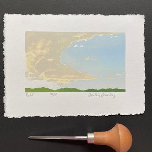 May include: A light blue and green print of a sky with clouds and a green horizon. The print is signed "Dealey  Gansberg" and numbered "9/20".