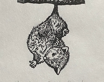 May include: Black and white linocut print of a small animal hanging upside down from a branch. The animal has a furry body and a small face. The branch is textured. The print is signed "Hiyah" and "Deuley Damsby".