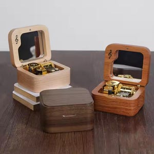 Puede incluir: Tres cajas de música de madera, dos abiertas y una cerrada. Las cajas abiertas revelan los mecanismos internos. Cada caja tiene un espejo dentro de la tapa y un símbolo de clave de sol. Los tonos de madera varían.