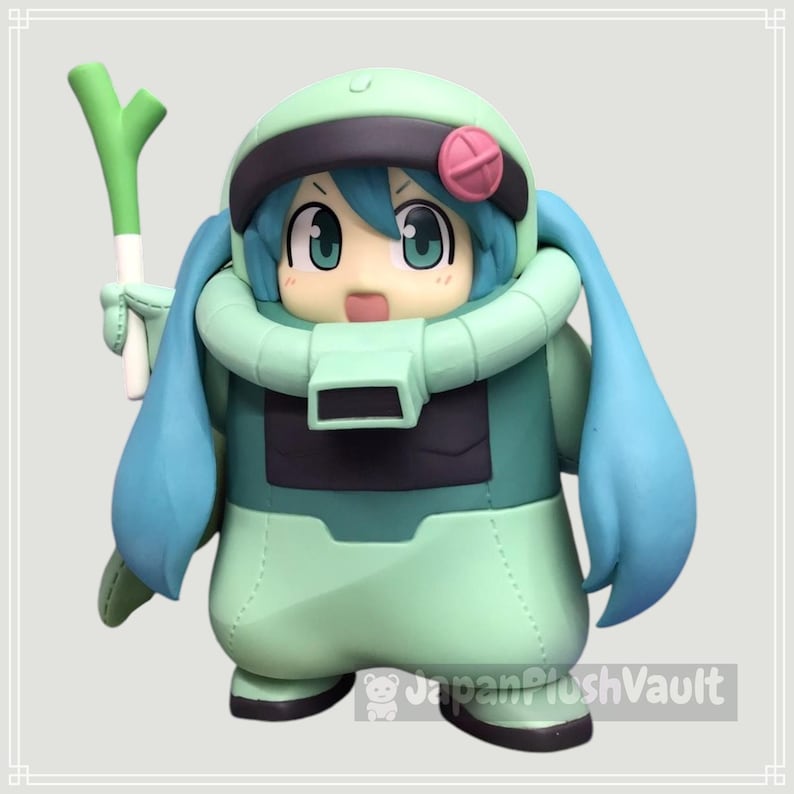 May include: A figurine of a character in a green and teal spacesuit-like outfit, holding a green and white vegetable. The character has blue hair, large eyes, and a pink accent on the helmet. The figurine has a cartoonish design.