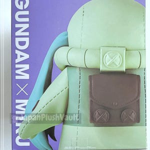May include: A plush toy figure in a box. The figure is light green with a brown pouch and blue accents. The box has the text "GUNDAM x MIKU" in white on a purple background.