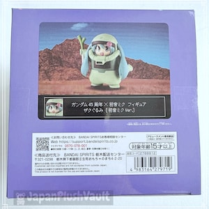 May include: A box featuring a figurine of a character in a green and white outfit with long blue hair. The box has Japanese text and a picture of the figurine. The background is a desert landscape.