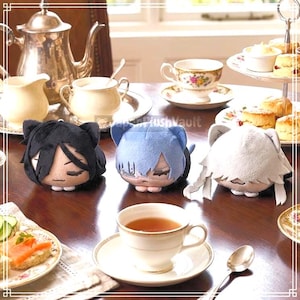 May include: Three plush cat-eared character heads arranged on a table. The left plush has black hair, the center plush has light blue hair with a bandage detail, and the right plush has white hair. Each plush features a soft, rounded design.