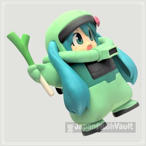 May include: A figurine of a cartoon character in a green and teal outfit, holding a green vegetable. The character has teal hair, large eyes, and a pink flower. The figure is in a dynamic pose, with a light gray background.