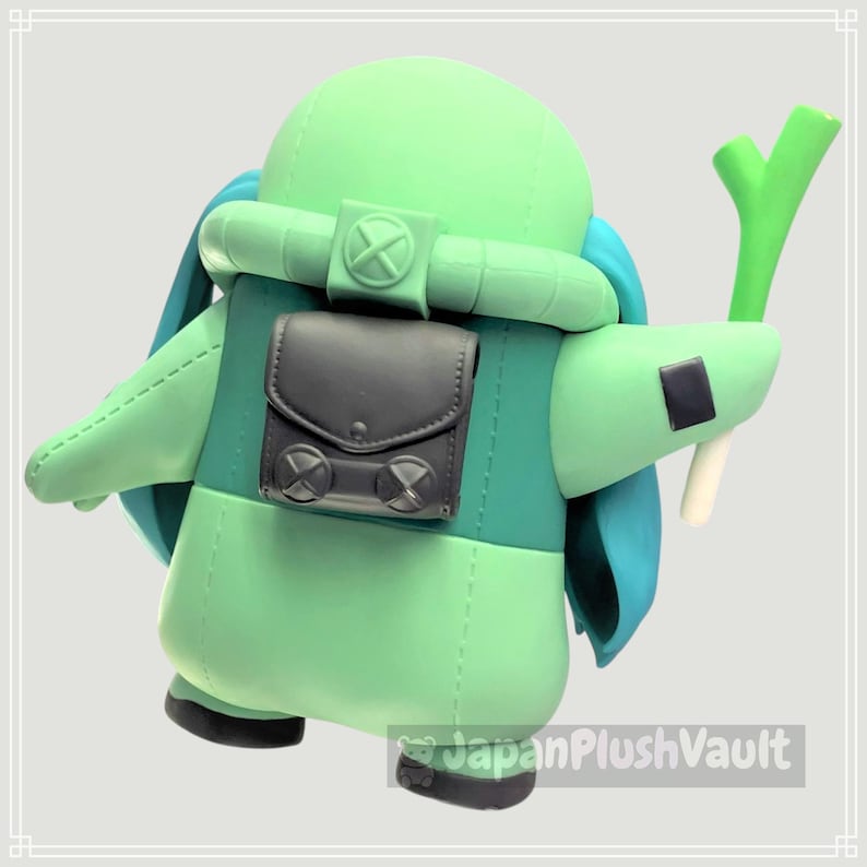 May include: A light green plush figure with a backpack and a green and white vegetable. The figure has a rounded head, a dark gray backpack, and blue accents. The figure is holding a green and white vegetable.