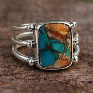 Peut inclure: Bague en argent avec une pierre rectangulaire turquoise, orange et dorée. La bague a un triple anneau avec de petites perles d'argent sur les côtés de la pierre. La pierre est sertie dans une lunette en argent.