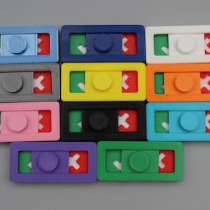 May include: Twelve colorful plastic fidget toys with a check mark, a circle, and an X on each. The toys are arranged in four rows of three.
