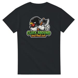 Puede incluir: Camiseta negra con un dibujo de un pollo de dibujos animados con una capucha negra y una hacha. El gráfico incluye el texto "CLUCK AROUND and find out" en verde y amarillo. El diseño está centrado en la parte delantera de la camiseta.