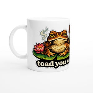 May include: White ceramic mug with a cartoon frog smoking a pipe, on a lily pad with a pink flower. The mug has the text "toad you so". The frog is brown and tan with yellow eyes.