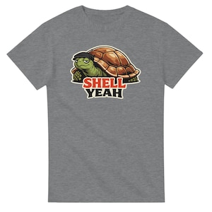 Könnte beinhalten: Graues T-Shirt mit einer Zeichentrickschildkröte, die eine schwarze Kappe trägt. Die Schildkröte hat einen grünen Kopf und einen braunen Panzer. Der Text "SHELL YEAH" ist rot und weiß darunter gedruckt.