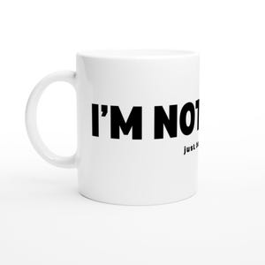May include: White ceramic mug with a curved handle. The mug features the text "I'M NOT" in bold black letters. Below the text is the word "just" in a smaller font. The mug is set against a white background.