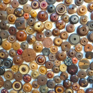 May include: A large collection of assorted circular wooden buttons in various shades of brown, tan, and grey. Each button features a central hole, with some displaying intricate carved patterns, smooth finishes, or layered wood grain textures.