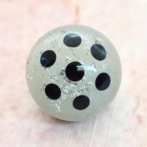 May include: A round, light gray decorative object with six large, evenly spaced black circles. The surface has silver flecks. The object is spherical and appears to be made of glass or a similar material.