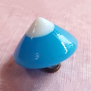 May include: A blue and white mountain-shaped button with a dark metal shank. The button features a glossy finish, with a white peak and a blue base. The button is likely for sewing or crafting projects.