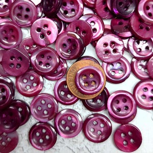 May include: A large collection of purple iridescent buttons with four holes each. The buttons are made of a shiny, pearlescent material.