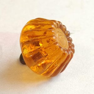 May include: A decorative amber-colored cabinet knob with a carved floral design. The knob has a rounded shape with a detailed, textured surface and a dark brown base. The knob is likely made of glass or resin.
