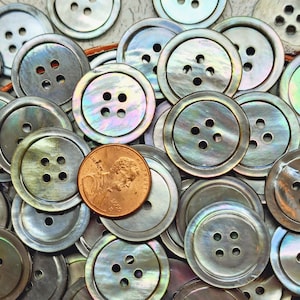 May include: A collection of iridescent mother-of-pearl buttons with four holes each. The buttons are arranged in a random pattern and a US penny is placed in the center of the image.