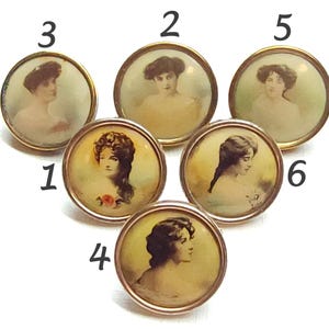 May include: Six antique brass-toned buttons with portraits of women. Each button features a different portrait, with a gold-colored border. The portraits are in soft, muted colors, with a vintage aesthetic.