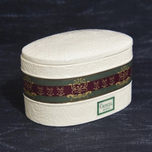 May include: White oval ceramic box with a green and burgundy patterned band and the text "Croscill" in gold lettering.