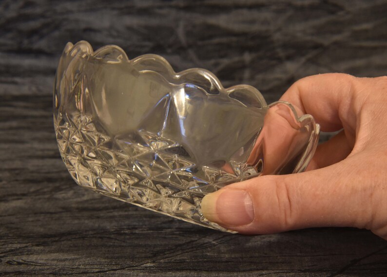 May include: A clear, scalloped-edge glass dish with a diamond-patterned base. The dish is held in a hand, showcasing its delicate design and transparency. The dish is likely for serving small portions.