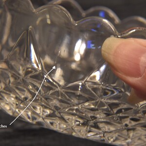 May include: Clear glass bowl with a scalloped rim and diamond-cut pattern. The bowl has small scratches on the surface. The bowl is held by a hand.