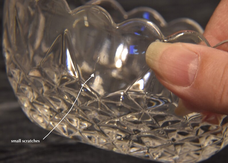 May include: Clear glass bowl with a scalloped rim and diamond-cut pattern. The bowl has small scratches on the surface. The bowl is held by a hand.