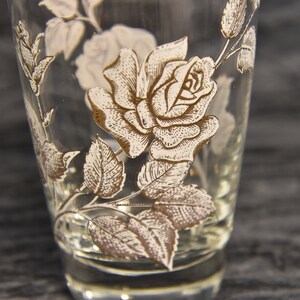 K&ouml;nnte beinhalten: Ein klares Glas mit einem goldenen und wei&szlig;en Rosenmuster. Die Rose ist mit Bl&auml;ttern und Stielen verziert.
