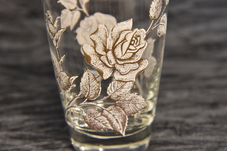K&ouml;nnte beinhalten: Ein klares Glas mit einem goldenen und wei&szlig;en Rosenmuster. Die Rose ist mit Bl&auml;ttern und Stielen verziert.