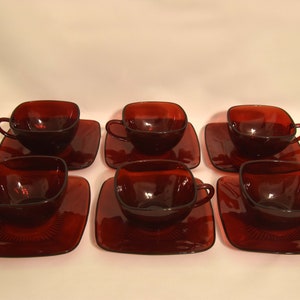 Puede incluir: Juego de seis tazas de té y platillos de vidrio rojo rubí. Las tazas y los platillos son de forma cuadrada y tienen una superficie ligeramente texturizada.