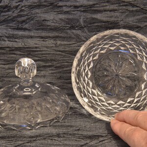 May include: A clear, cut-glass serving bowl with a matching lid. The lid has a round, knob-like handle. The bowl and lid are decorated with a diamond pattern. The bowl is approximately 6 inches in diameter.