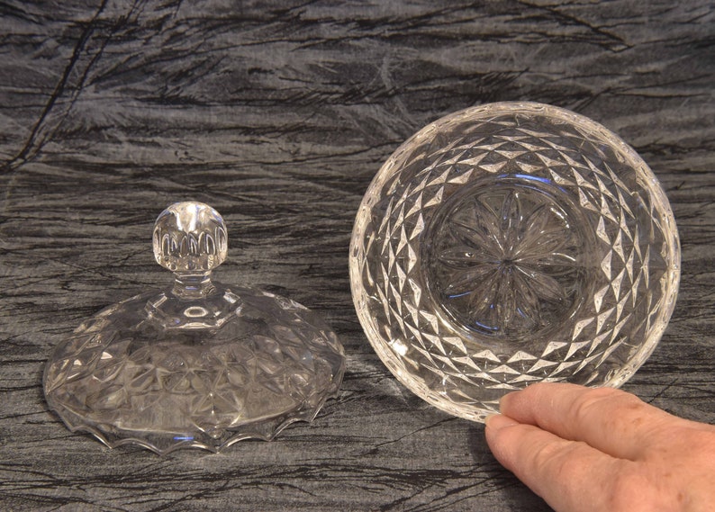 May include: A clear, cut-glass serving bowl with a matching lid. The lid has a round, knob-like handle. The bowl and lid are decorated with a diamond pattern. The bowl is approximately 6 inches in diameter.
