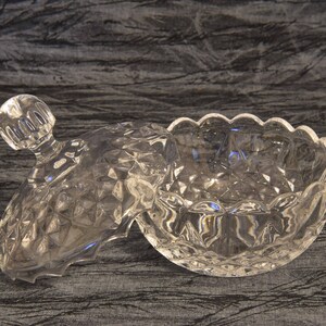 May include: A clear, cut-glass candy dish with a lid. The dish has a diamond pattern and a scalloped edge. The lid has a knob handle. The dish is open, revealing its interior. The overall theme is vintage glassware.