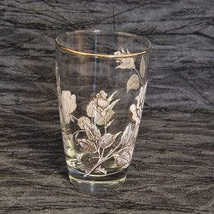 K&ouml;nnte beinhalten: Ein klares Glas mit goldfarbenem Rand und einem wei&szlig;en Blumenmuster. Die Blumen sind Rosen mit Bl&auml;ttern und Stielen.