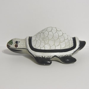 May include: A ceramic turtle figurine with a white shell featuring a scale pattern. The turtle has a black and white body with a detailed head, and is likely a decorative item.