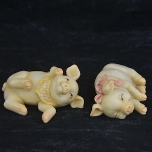 Vintage Resin Pig Figurines. Small Pig Figurines Lying Down, one with a Pink Bow, the other with a Handkerchief. Smiling Shelf Sitter Pigs.