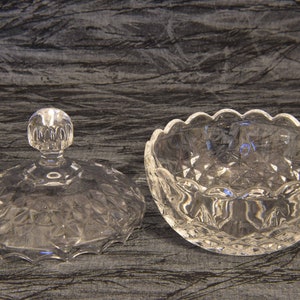 May include: A clear, cut-glass candy dish with a lid. The dish has a scalloped edge and a diamond pattern. The lid has a round knob. The dish is designed to hold small candies or other treats.