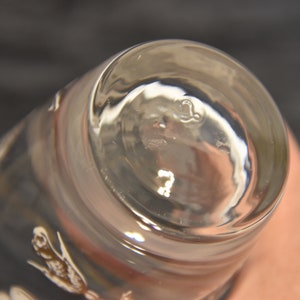 K&ouml;nnte beinhalten: Nahaufnahme des Bodens eines klaren Glases mit einem kleinen, einge&auml;tzten Buchstaben "L" am Boden.